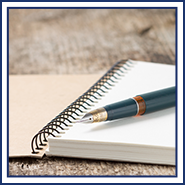 Open notebook and pen sit on a wooden surface