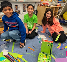 Three smiling students pause while building leprechaun traps