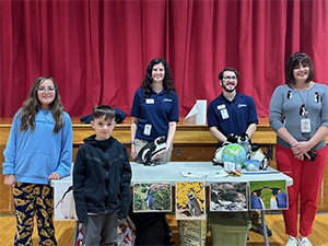 Students and adults around a table with penguins on it