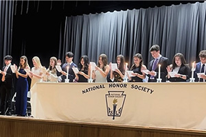 Students holding papers and standing behind a table that reads National Honor Society