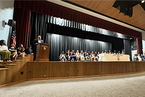Students sitting on stage while an adult talks