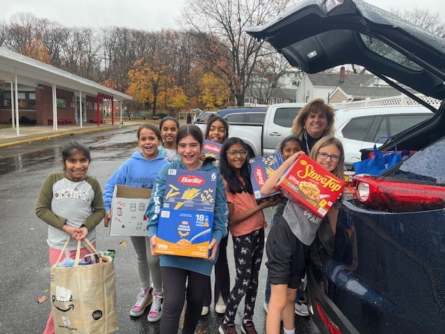 Students smiling for the camera while loading food supplies into a car
