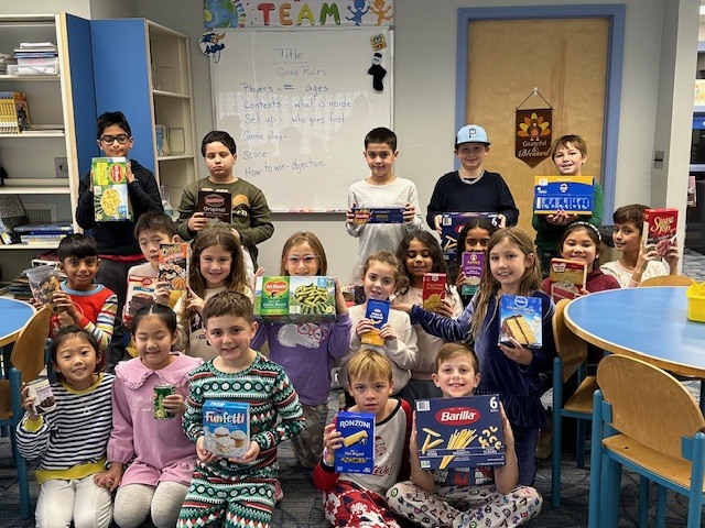 Classroom full of students smiling for the camera with food items for the food drive