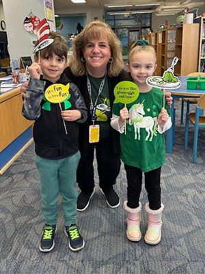 Teacher with two students holding a Dr. Seuss hat and green eggs and ham