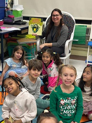 Teacher holding a book up while students smile at camera