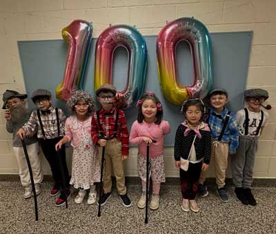 Students dressed as elders under a sign that reads 100