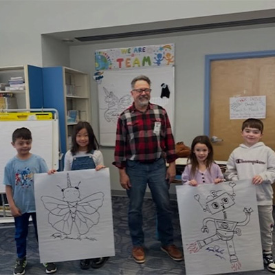 Author standing with students holding drawings